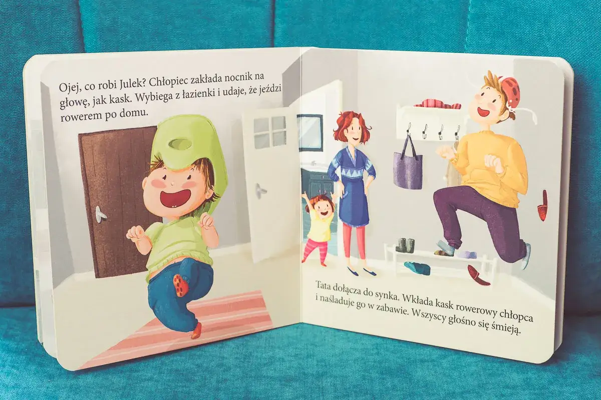 Ilustracja z książki o emocjach: chłopiec zakłada nocnik na głowę jak kask, udając jazdę rowerem. Tata dołącza do zabawy.