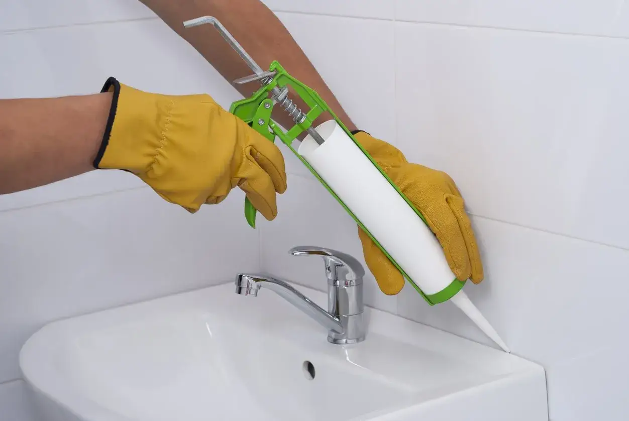 Hände mit Handschuhen dichten den Spalt am Waschbecken ab. Die Frage ist: wie lange muss silikon trocknen dusche?