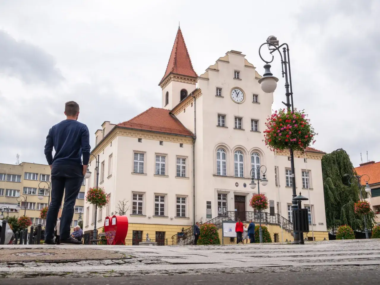 Mężczyzna podziwia ratusz, jedną z głównych atrakcji Trzebnicy. W tle widać zegar i czerwone serce.