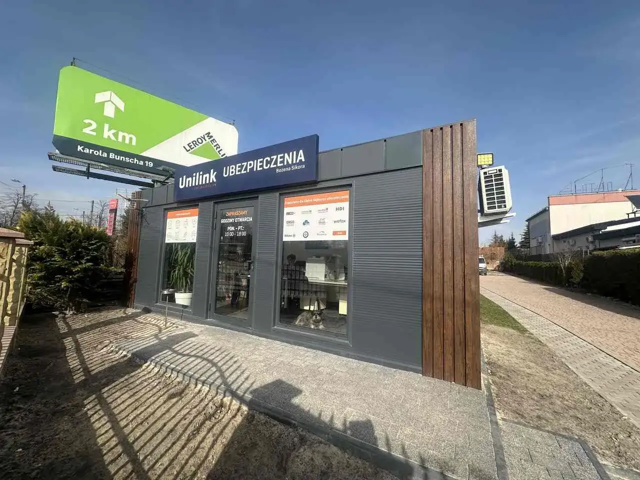 Nowoczesny punkt Unilink Ubezpieczenia z tablicą informacyjną i billboardem w tle.
