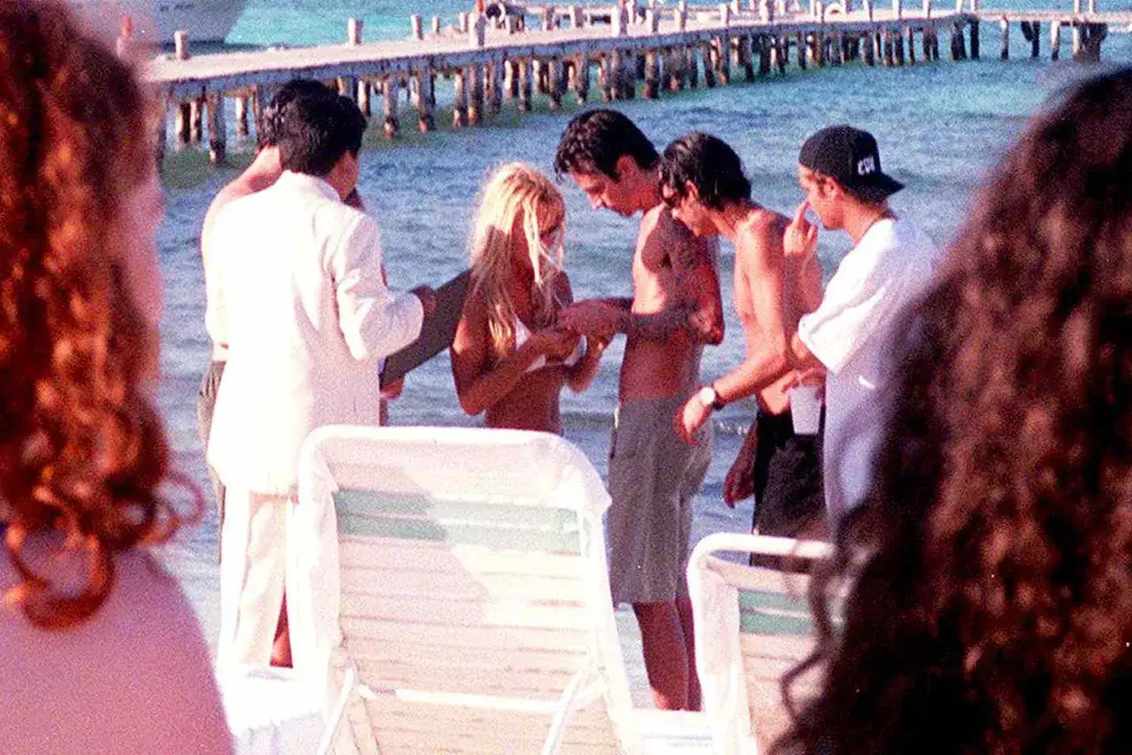 Pamela Anderson i Tommy Lee na plaży, otoczeni przyjaciółmi, w tle drewniane molo.