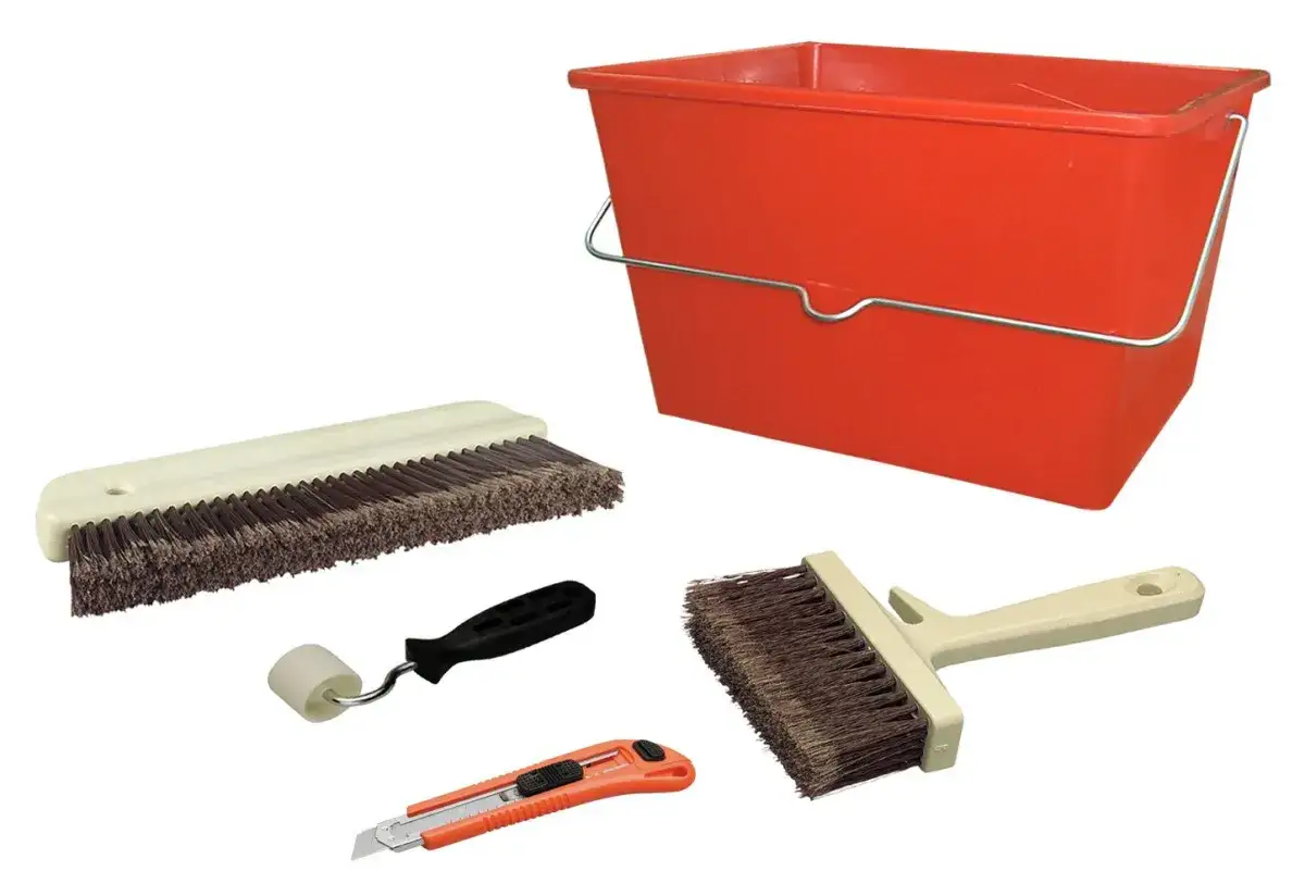 Herramientas para pintar: cubo rojo, brocha ancha, rodillo pequeño, cúter y cepillo. ¡Todo listo para los pasos para pintar una pared!