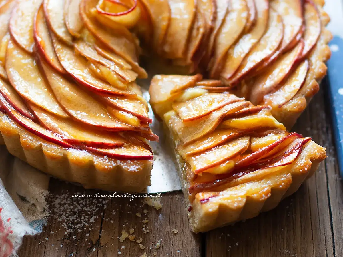 Una deliziosa crostata di mele, con fette di mela lucide disposte a spirale su una base dorata. Una fetta è stata tolta, rivelando la morbidezza.