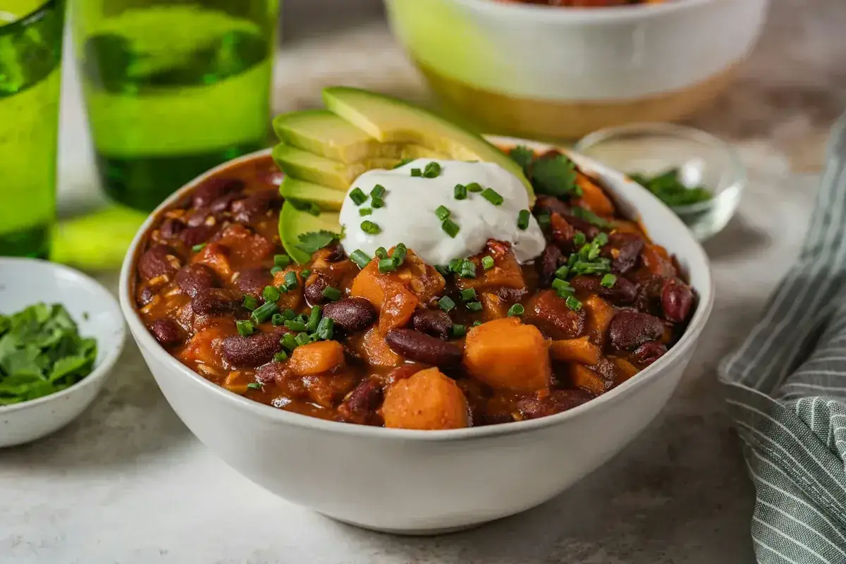 En skål med godaste chili con carne, toppad med gräddfil, avokado och gräslök. Serveras med gröna glas i bakgrunden.