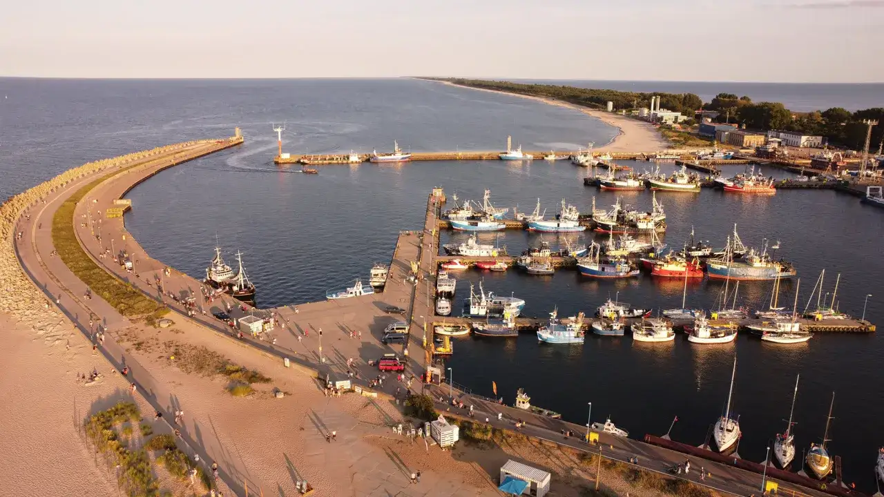 Port rybacki we Władysławowie, pełen łodzi i statk&oacute;w, z falochronem i plażą w tle.