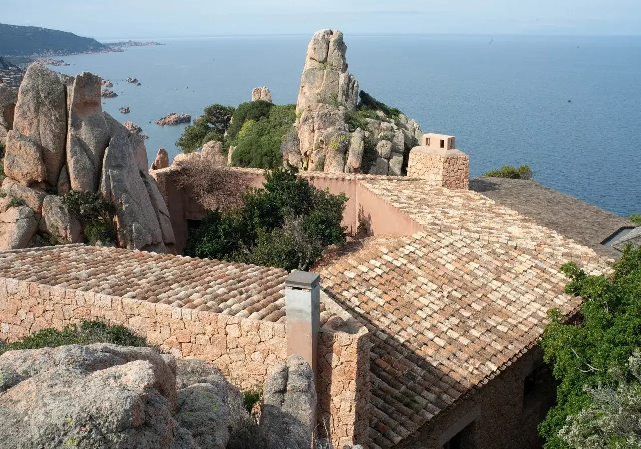 Un paesaggio roccioso e marino con tetti in cotto, tipici delle opere di Alberto Ponis, si fonde con la natura selvaggia.