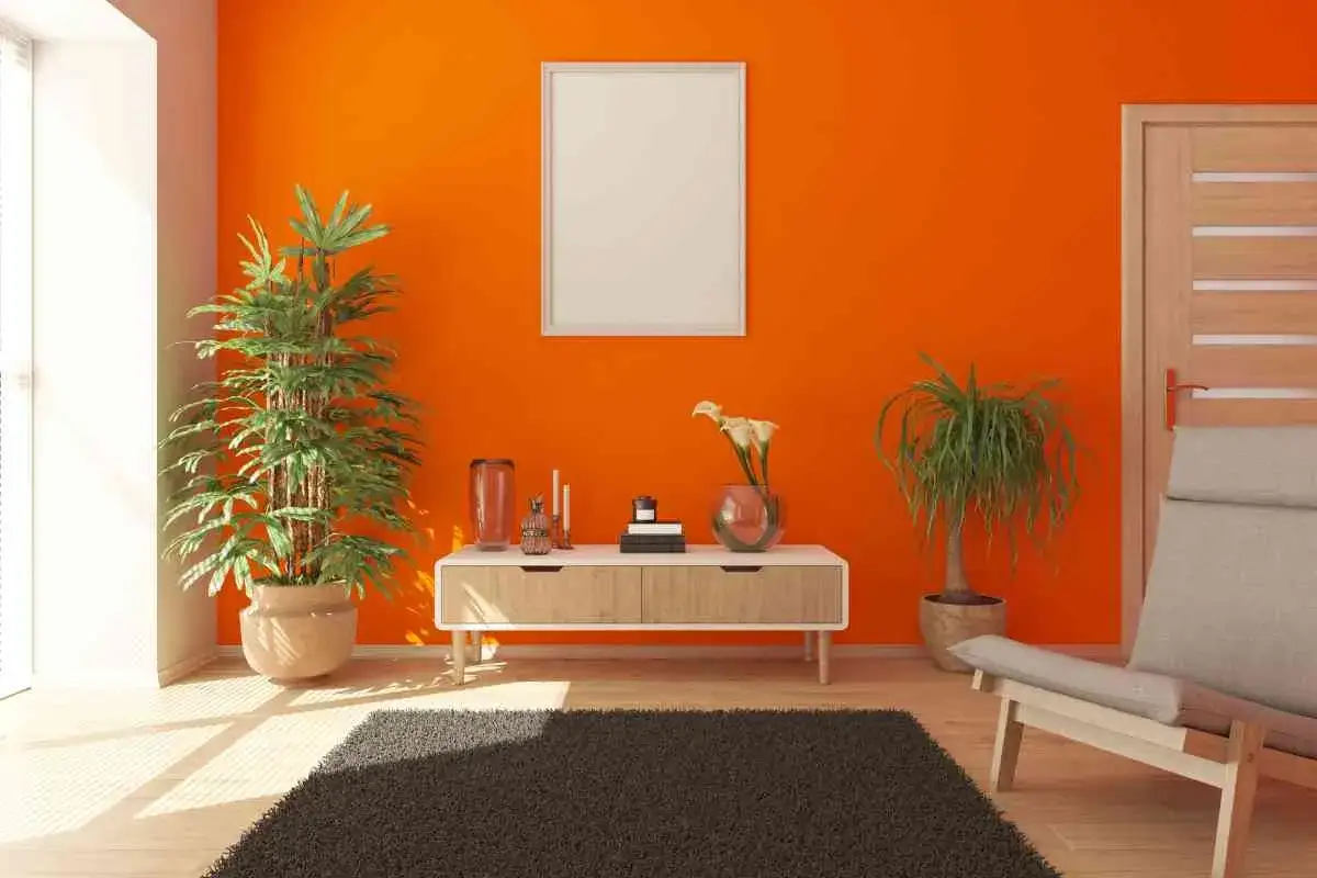 Arredamento moderno con pareti arancioni vivaci. Un tavolino con piante e decorazioni, un quadro vuoto e una poltrona completano l'ambiente, suggerendo idee per colori da abbinare all'arancione pareti.