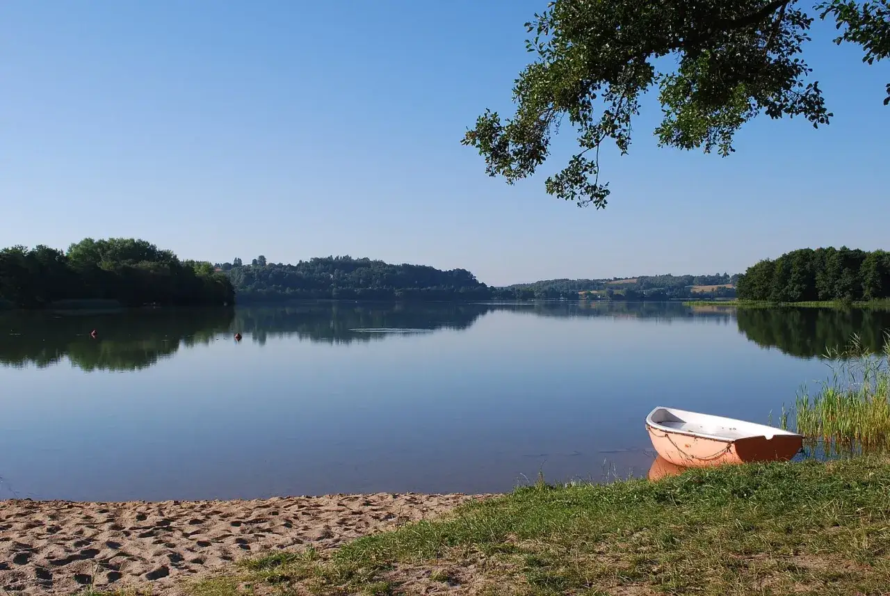 Spokojne jezioro Kłodno z ł&oacute;dką przy brzegu, otoczone zielonymi wzg&oacute;rzami i drzewami.