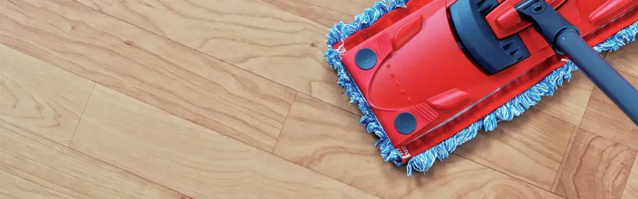 A red mop with blue fringe glides across a light wood-grain vinyl floor, making cleaning easy and efficient.