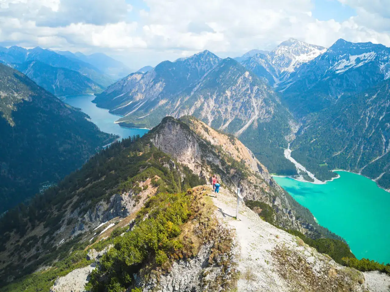 Zwei Wanderer genie&szlig;en die atemberaubende Aussicht auf den t&uuml;rkisfarbenen Plansee und die umliegenden Berge. Ein perfekter Tag zum Plansee wandern.