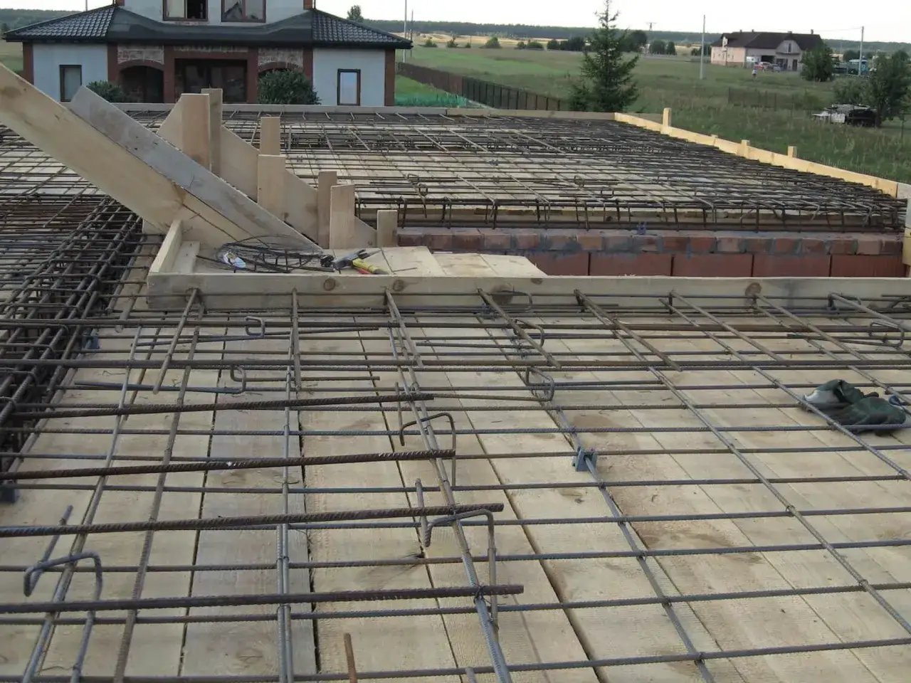 Siatka zbrojeniowa na drewnianym deskowaniu, przygotowana do wylania stropu betonowego 100m2. W tle dom i krajobraz.