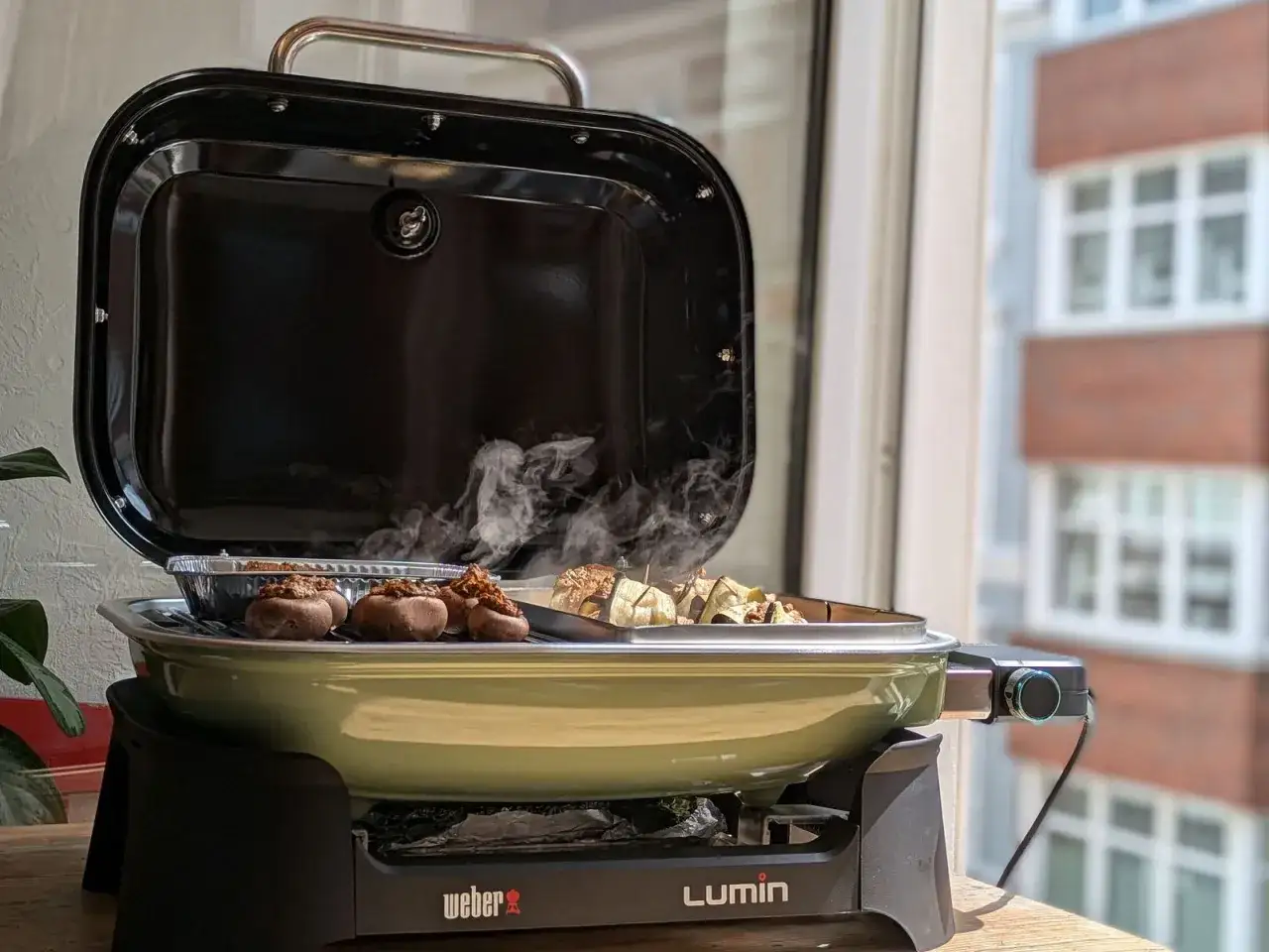 Lecker gef&uuml;llte Champignons und Gem&uuml;se brutzeln auf dem Balkon. Der Weber Lumin Grill dampft und verstr&ouml;mt Vorfreude auf das Grillen.
