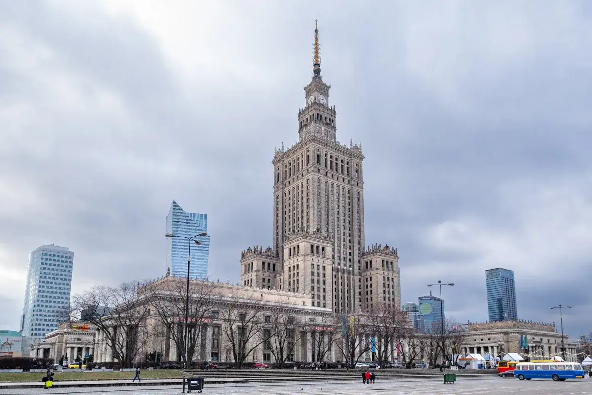 Pałac Kultury i Nauki oraz nowoczesne wieżowce w centrum Warszawy. Widać też autobus i ludzi spacerujących po placu. Idealne atrakcje Warszawa dzisiaj!