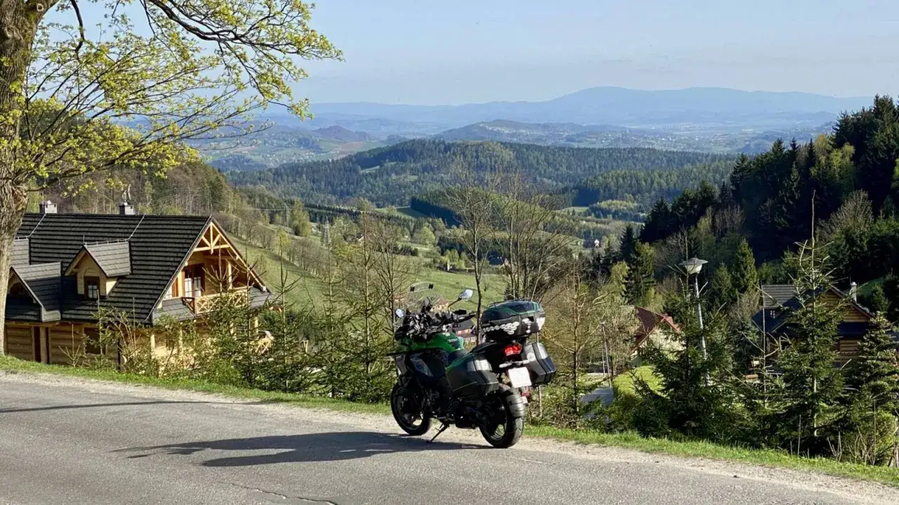 Zielony motocykl zaparkowany na poboczu drogi z widokiem na malownicze wzg&oacute;rza i lasy. Idealne miejsce na odkrywanie tras motocyklowych Czech.
