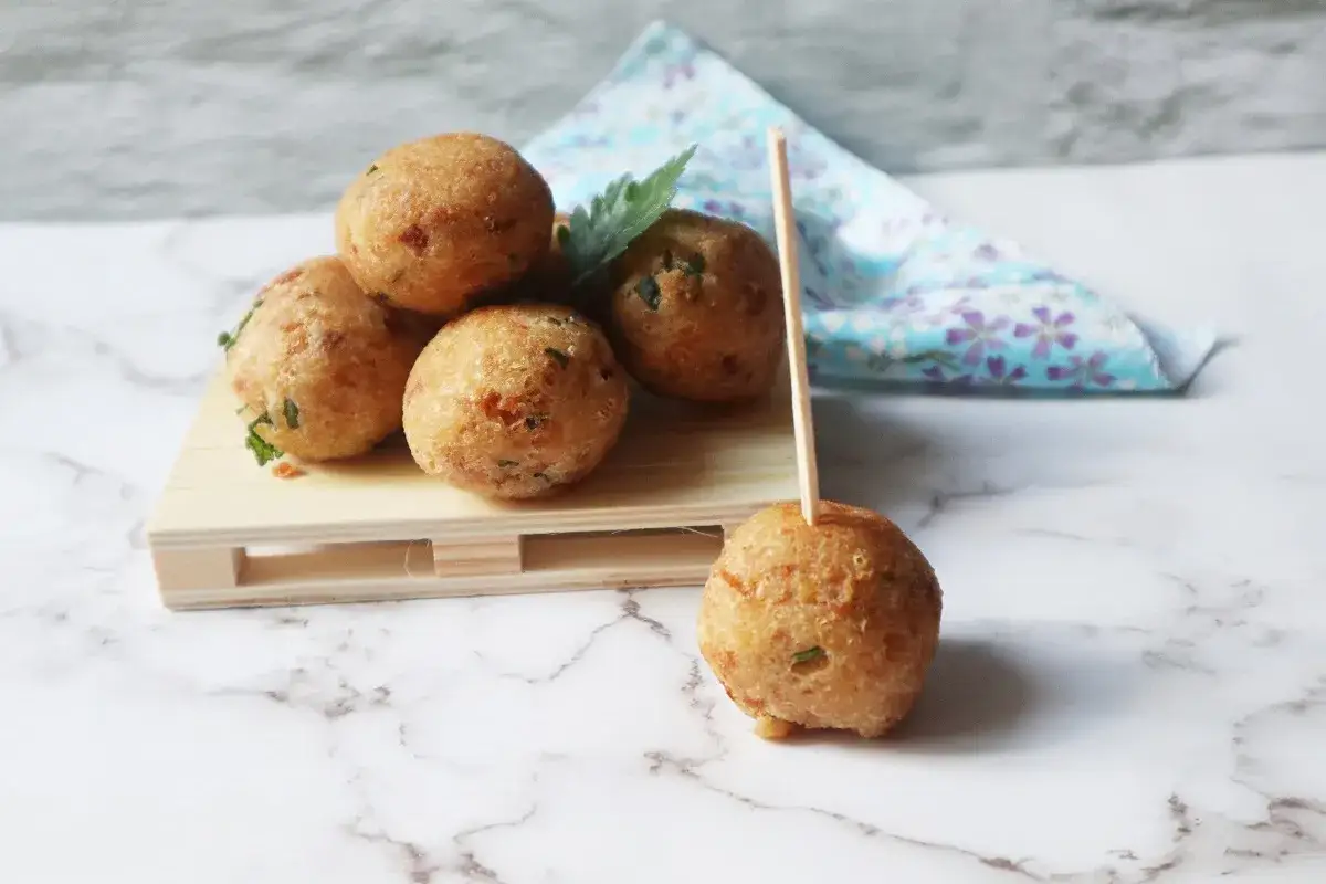 Deliziose polpette di pane dorate, alcune impilate su un piccolo vassoio di legno, una infilzata su uno stecchino.