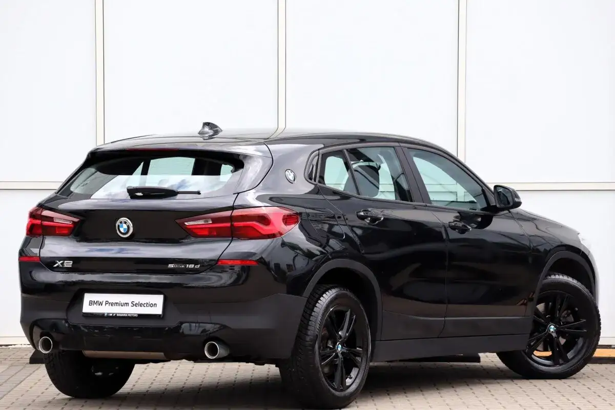 Czarny BMW F39 X2 sDrive 18d z czarnymi felgami, zaparkowany przed białym budynkiem.