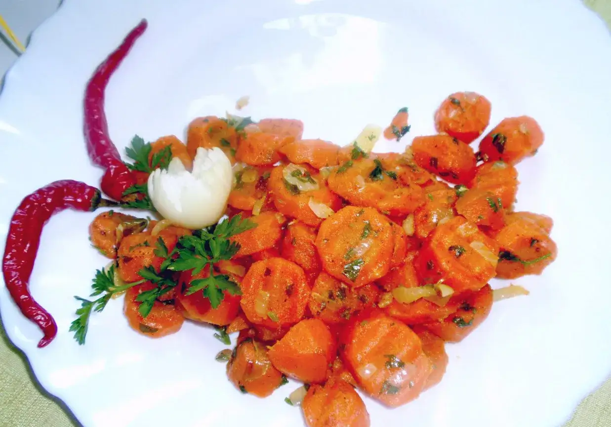 Gotowana marchewka z chili i natką pietruszki, podana na białym talerzu.