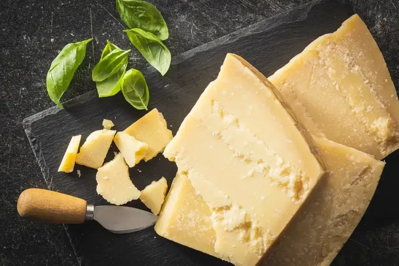 Kawałki Grana Padano i parmezanu, świeża bazylia i nóż do sera na czarnej desce. Idealne do makaronu i sałatek.