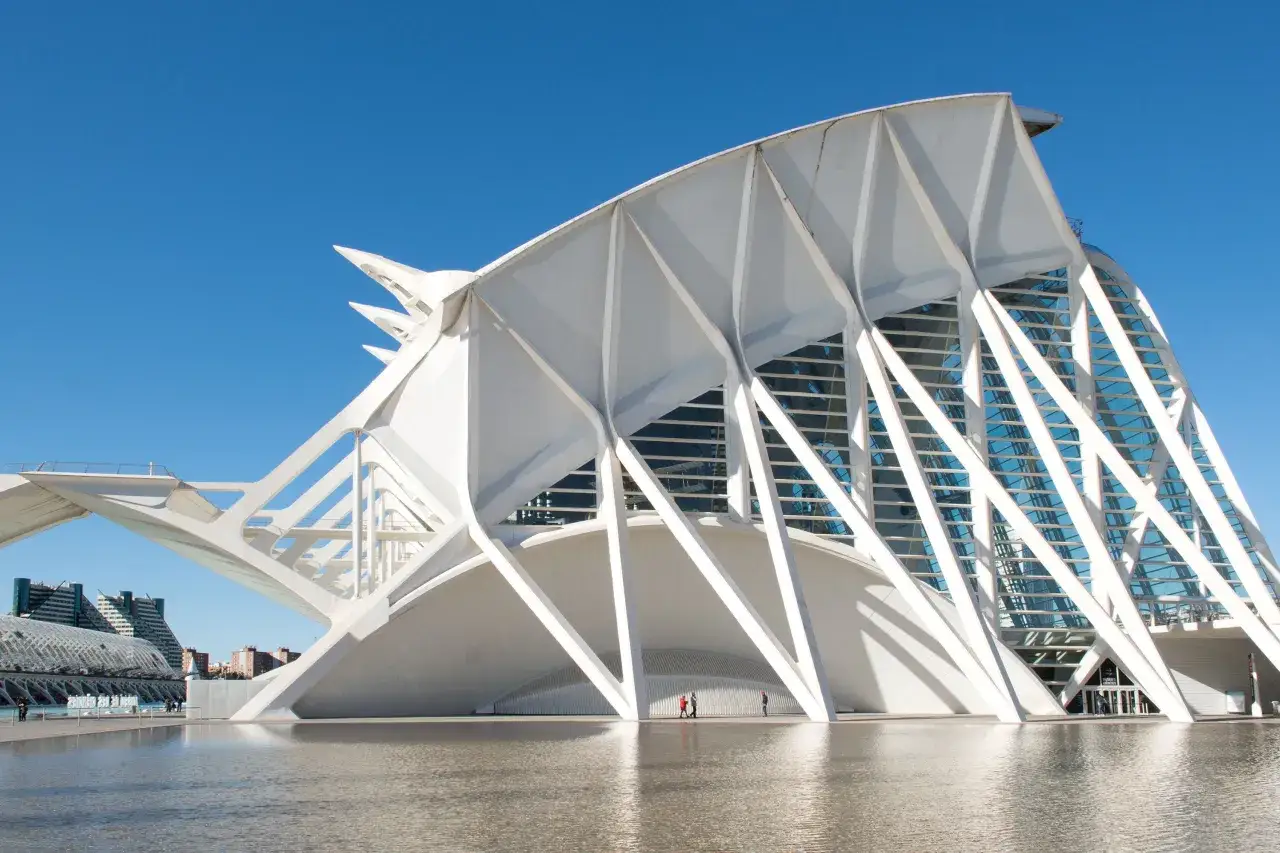 La futurista arquitectura en Valencia, con su diseño blanco y cristalino, se refleja en el agua serena bajo un cielo azul.