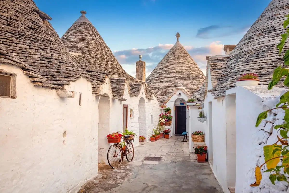 Urokliwa uliczka w Alberobello z białymi domkami trulli i kamiennymi dachami. Rower ozdobiony kwiatami czeka na przejażdżkę.