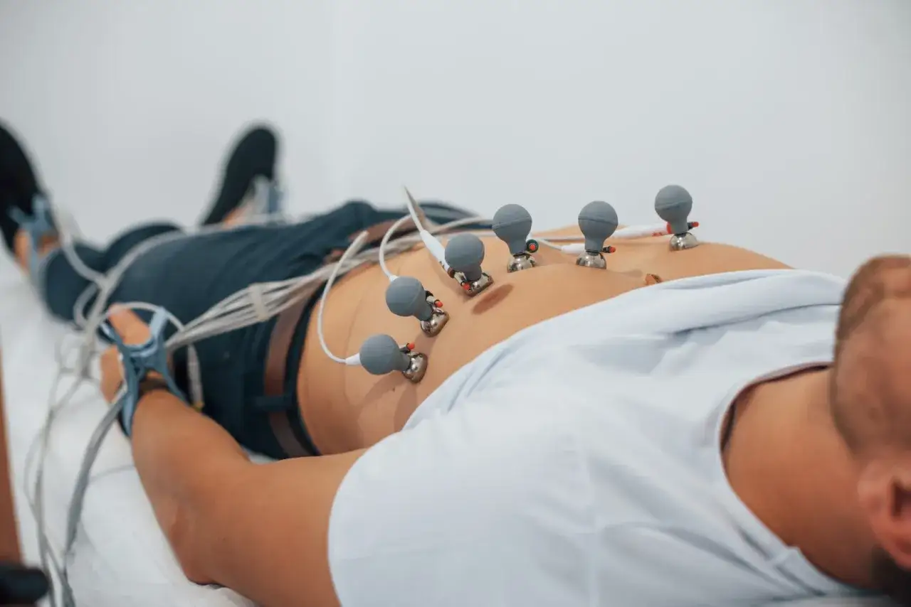Mężczyzna leży na plecach, podłączony do aparatury do badania ekg serca. Elektrody na klatce piersiowej i kończynach.