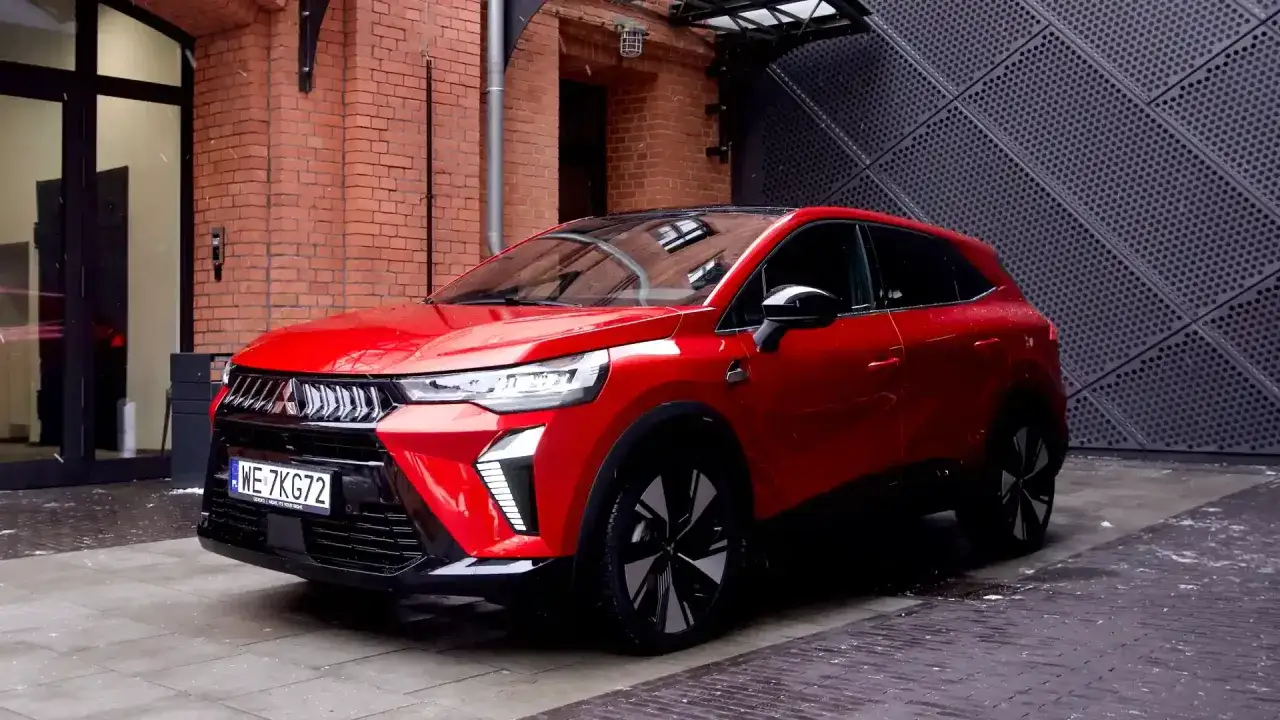 Czerwony SUV Mitsubishi, jeden z nowoczesnych **mitsubishi modele**, zaparkowany na tle ceglanej ściany i metalowej fasady.