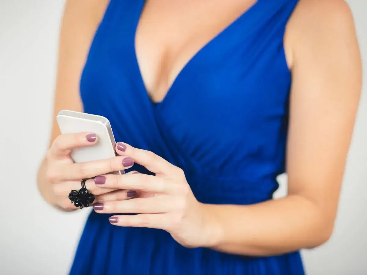 Kobieta w granatowej sukience wybiera jaki kolor paznokci pasuje do stylizacji, trzymając telefon.