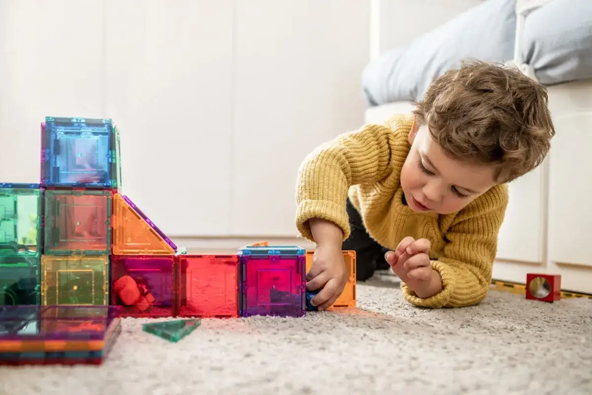 Ni&ntilde;o de **infantil 3 a&ntilde;os** concentrado construyendo con bloques magn&eacute;ticos de colores.