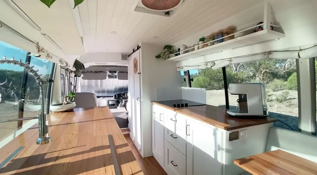 Interior de un minibus vivienda con cocina completa, cafetera y grifo de dise&ntilde;o.