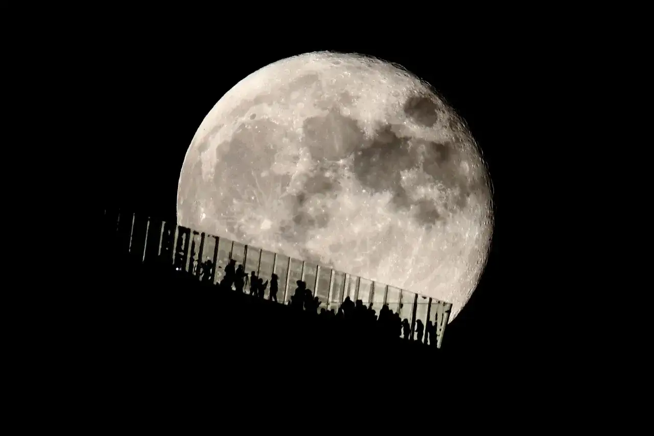 Menschen stehen auf einer Aussichtsplattform und fotografieren den Vollmond mit ihrem Handy.