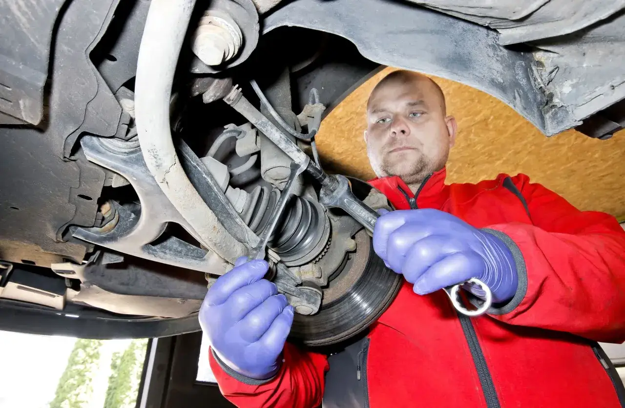 Mechanik w niebieskich rękawiczkach dokręca śrubę przy kole. Sprawdza, czy wymiana drążka kierowniczego cena jest adekwatna do jakości usługi.