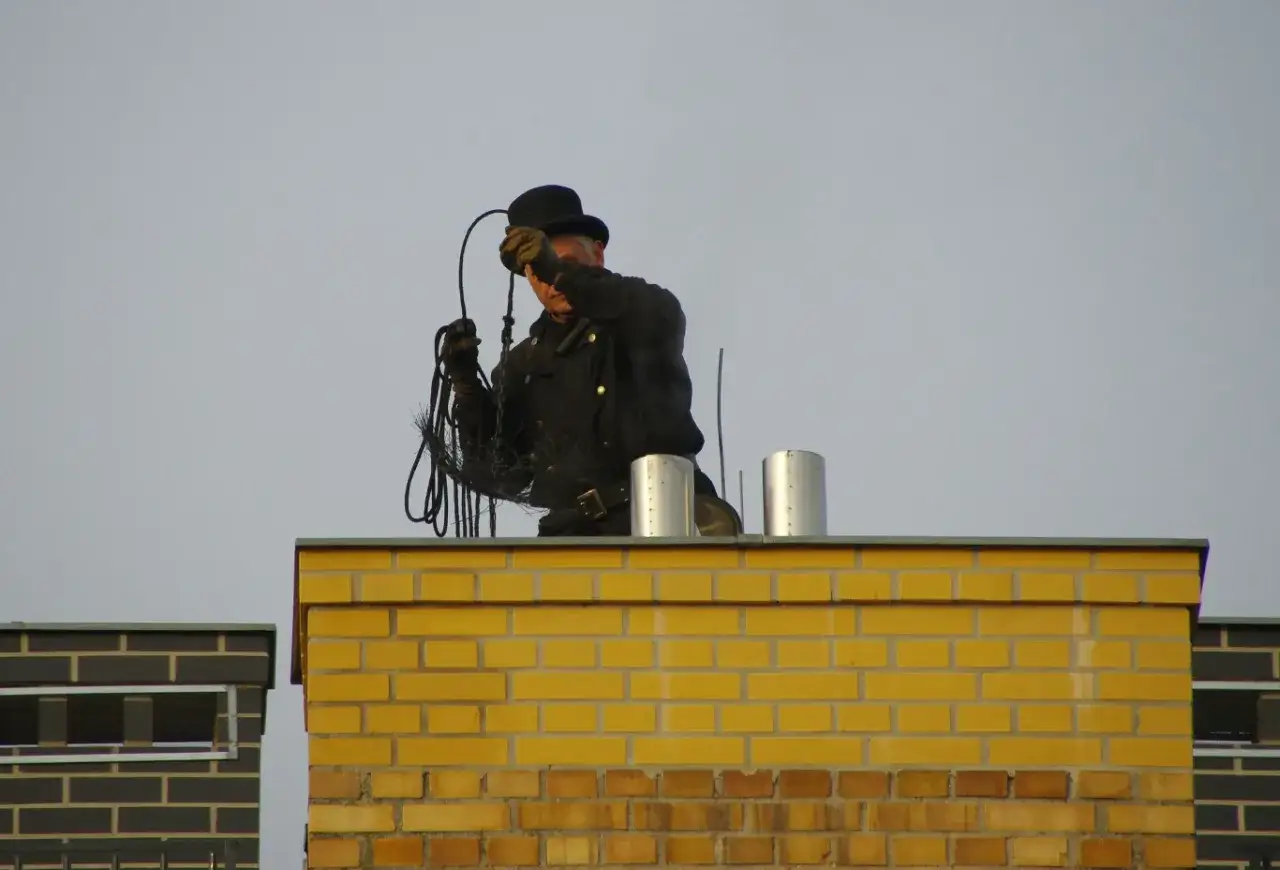 Kominiarz w cylindrze na dachu z czyścikiem. Chcesz wiedzieć, jak zostać kominiarzem?