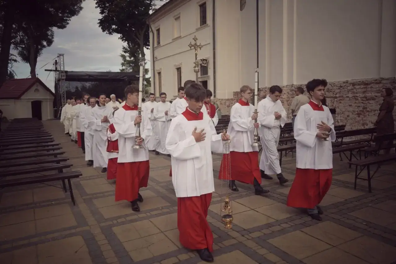 Chłopcy w albach i czerwonych szatach niosą świece i kadzielnicę, przygotowując się do procesji. Ich kroki wyznaczają rytm pieśni na wejście.