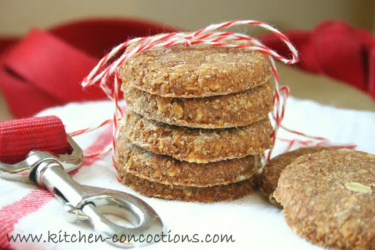 Pila de galletas caseras para perros, atadas con hilo rojo y blanco. Un gancho de metal y tela roja al lado.