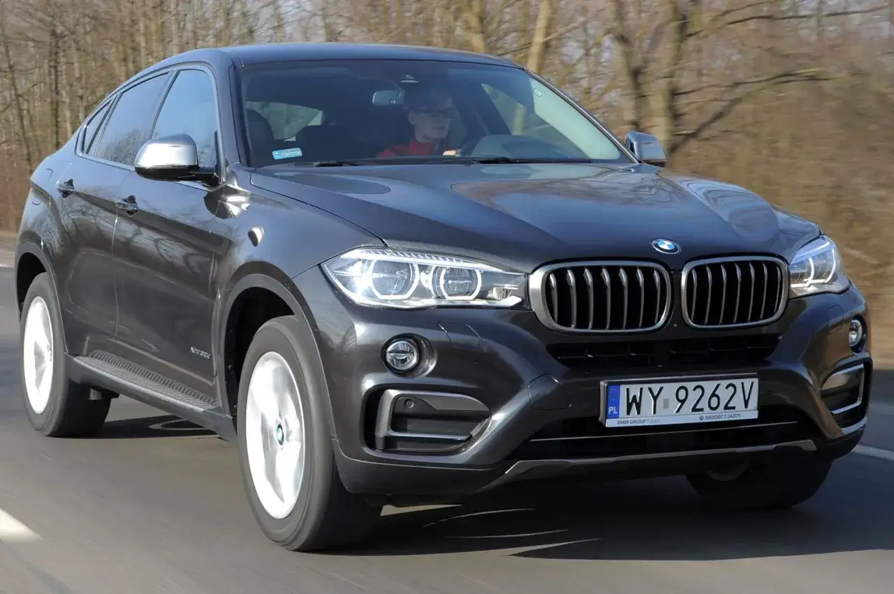 Ciemnoszary BMW F16 z kierowcą za kierownicą jedzie po drodze.