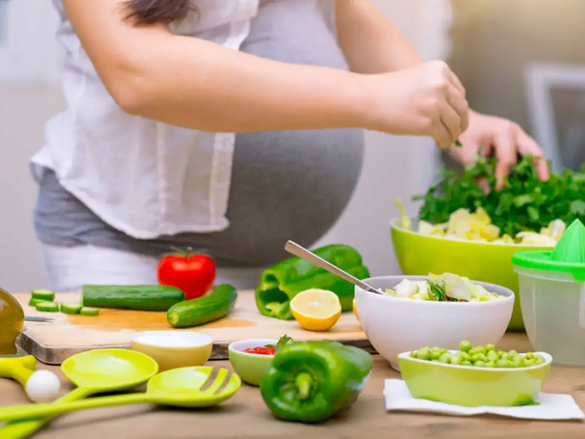 Kobieta w ciąży przygotowuje zdrową sałatkę. Dba o dietę, szukając informacji, jak schudnąć w ciąży, stawiając na świeże warzywa.