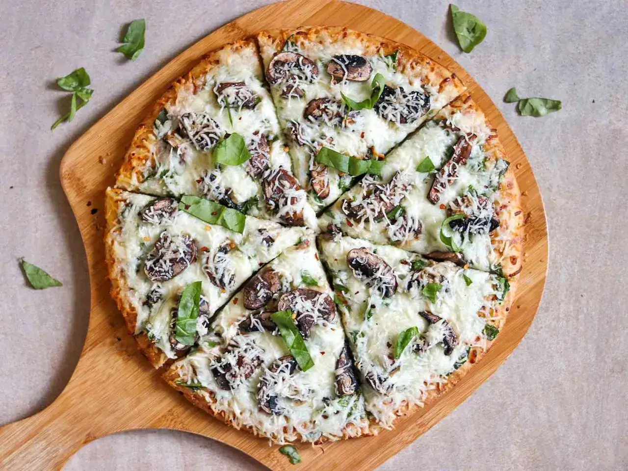 Pyszna pizza z pieczarkami do pizzy, serem i bazylią, podana na drewnianej desce.