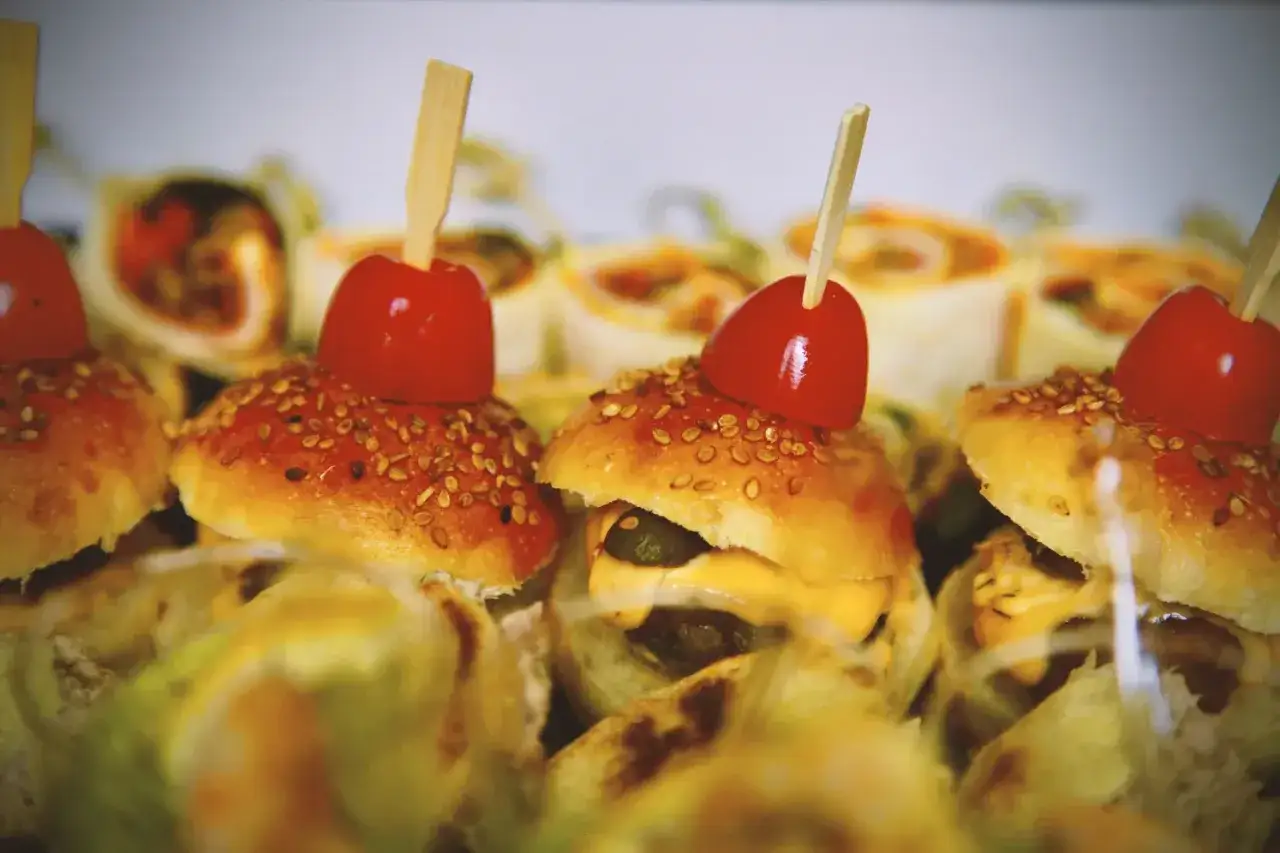 Mini burgery z pomidorkiem i sezamem, idealne jako koreczki na przyjęcie. Widać też zawinięte rolady.