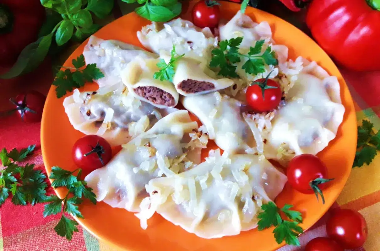 Pyszne pierogi meksykańskie z mięsnym farszem, posypane cebulką i udekorowane pomidorkami koktajlowymi i natką pietruszki.