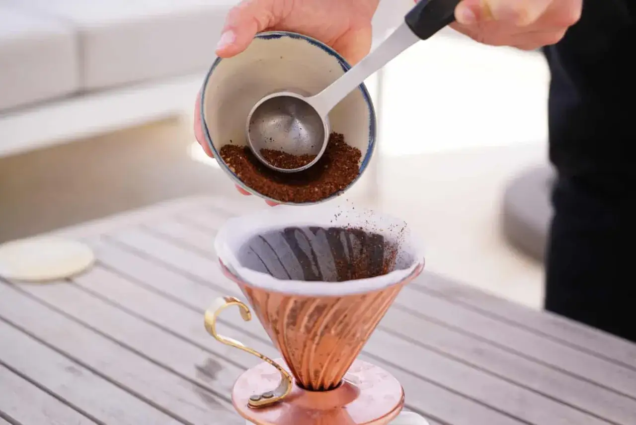 Frisch gemahlener Kaffee rieselt aus einer Schale in einen Kupfer-Filterhalter. Der Weg zum perfekten Filterkaffee beginnt hier.