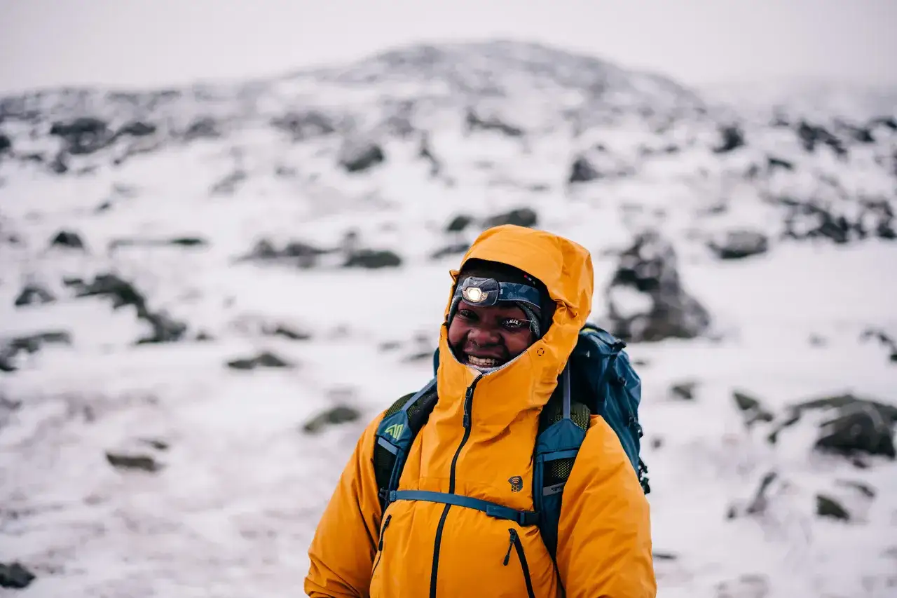 Un sourire éclatant lors d'une randonnée dans la neige. Vêtu d'une veste orange vif et d'un sac à dos, il est prêt pour l'aventure hivernale.