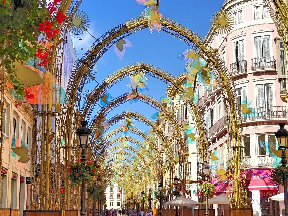 Festliche B&ouml;gen schm&uuml;cken die malaga altstadt. Bunte Bl&auml;tter und Blumen zieren die Gassen unter blauem Himmel.