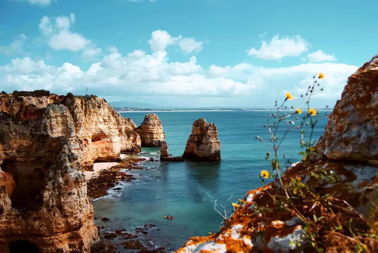Acantilados dorados y mar turquesa en el Algarve. Un kayak navega cerca de las rocas, perfecto para tu plan de Algarve en 7 d&iacute;as.