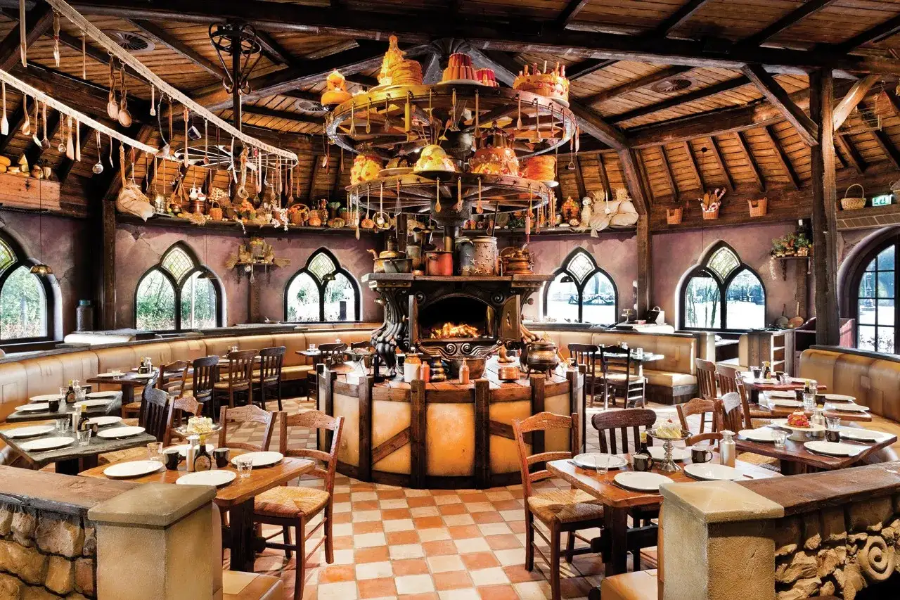 Gemütliches Efteling Restaurant mit rustikalen Holztischen, Kamin und einer drehenden Kuchenpyramide.