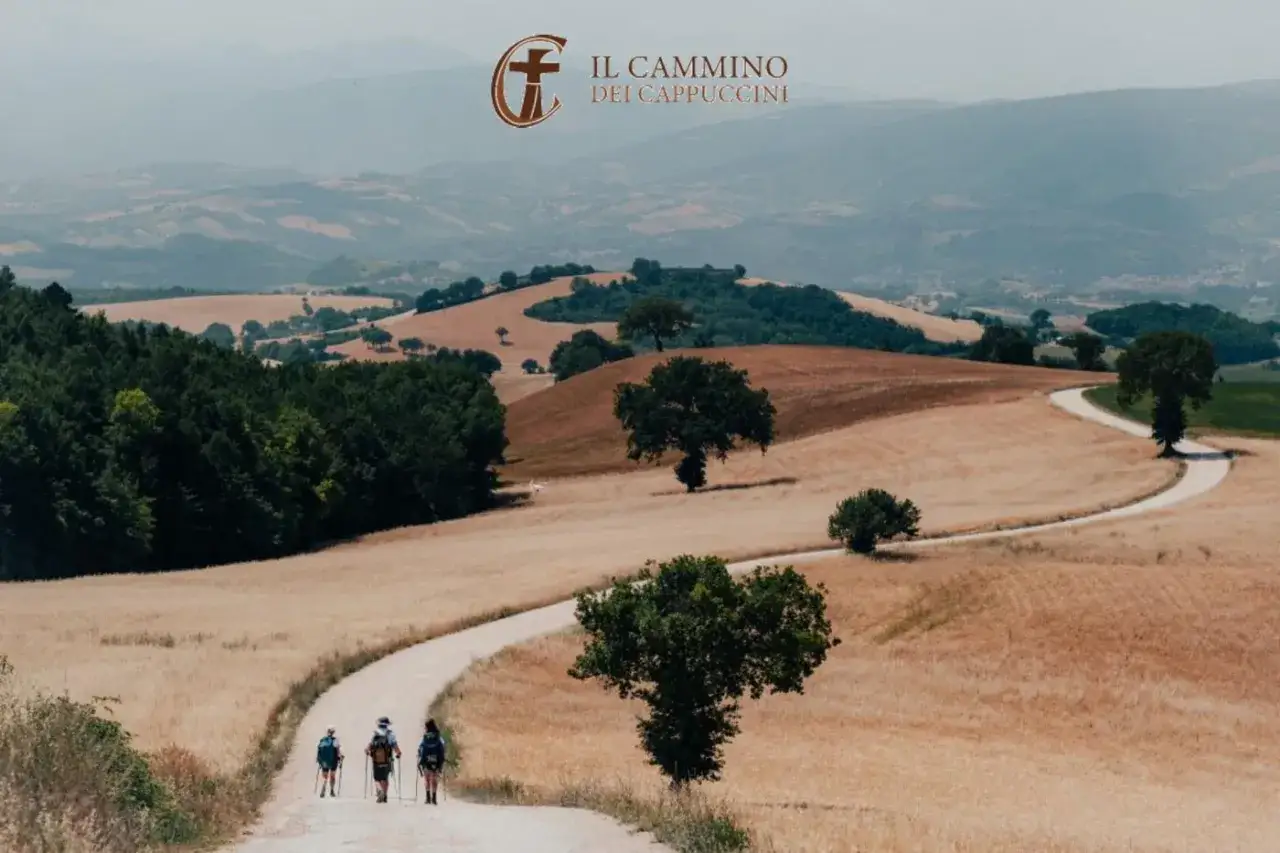 Tre escursionisti percorrono un sentiero sinuoso attraverso colline dorate, parte del cammino dei cappuccini.