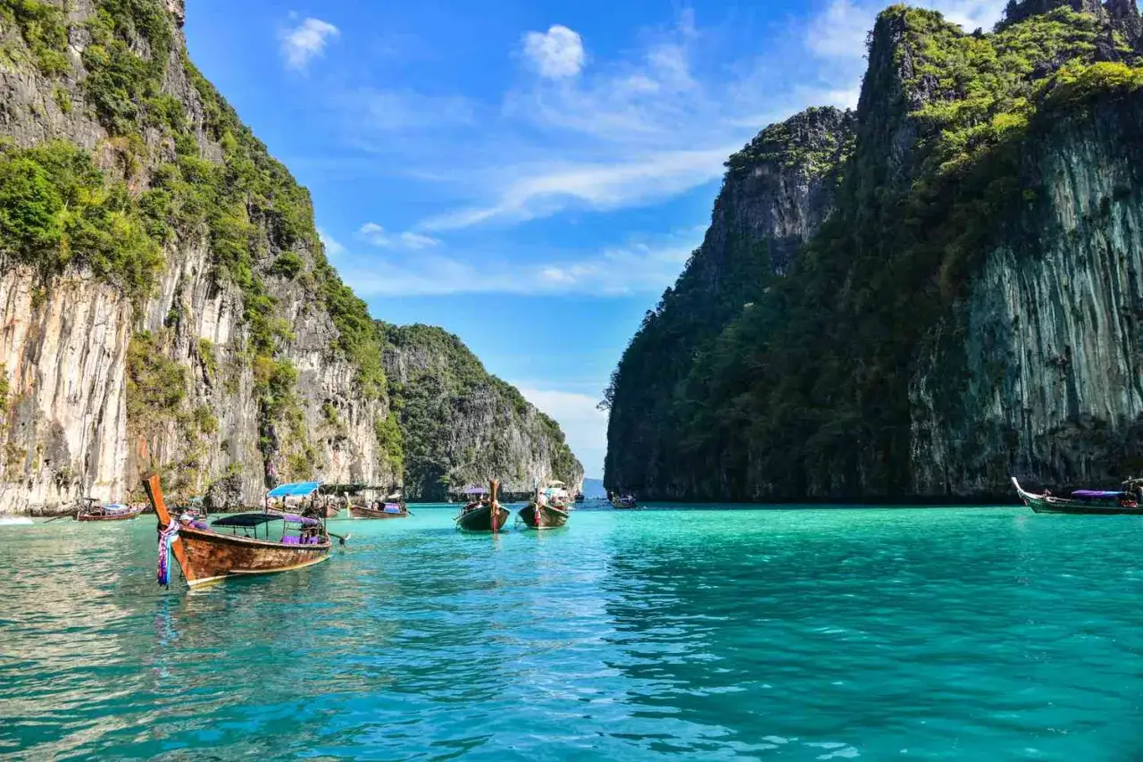 Traumhaftes Thailand im November: Türkisblaues Wasser umspült steile, grüne Felsen. Longtail-Boote schaukeln sanft auf der Bucht.
