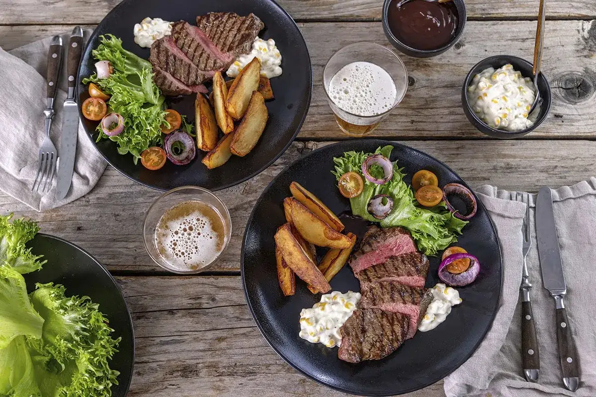 Tv&aring; tallrikar med saftig grillad biff, klyftpotatis, sallad och tomater. Perfekt f&ouml;r en mysig kv&auml;ll med n&aring;got gott att grilla.