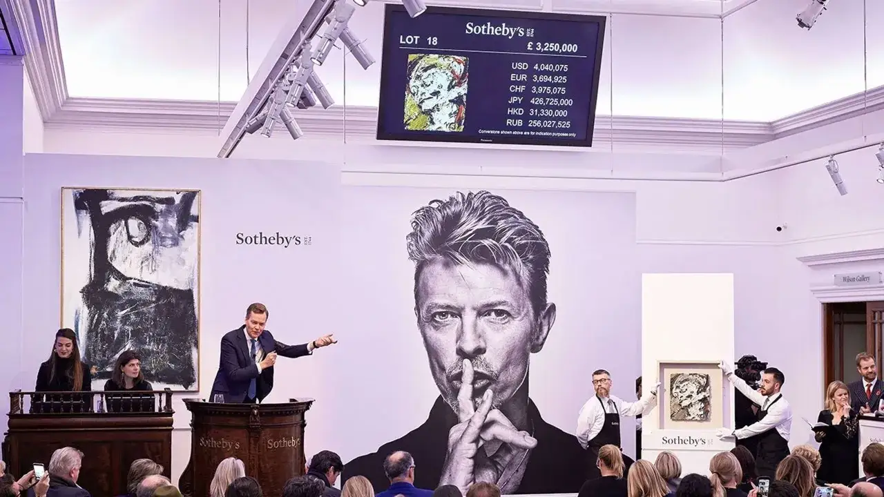 An auctioneer at Sotheby's presents a painting, with a large portrait of David Bowie behind him. A screen displays the lot number and a price of £3,250,000, illustrating what is fair market value.