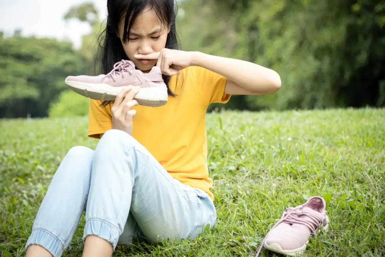 Niña con expresión de asco huele zapatilla, quizás por el sudor de los pies de niños tras un día de juegos.