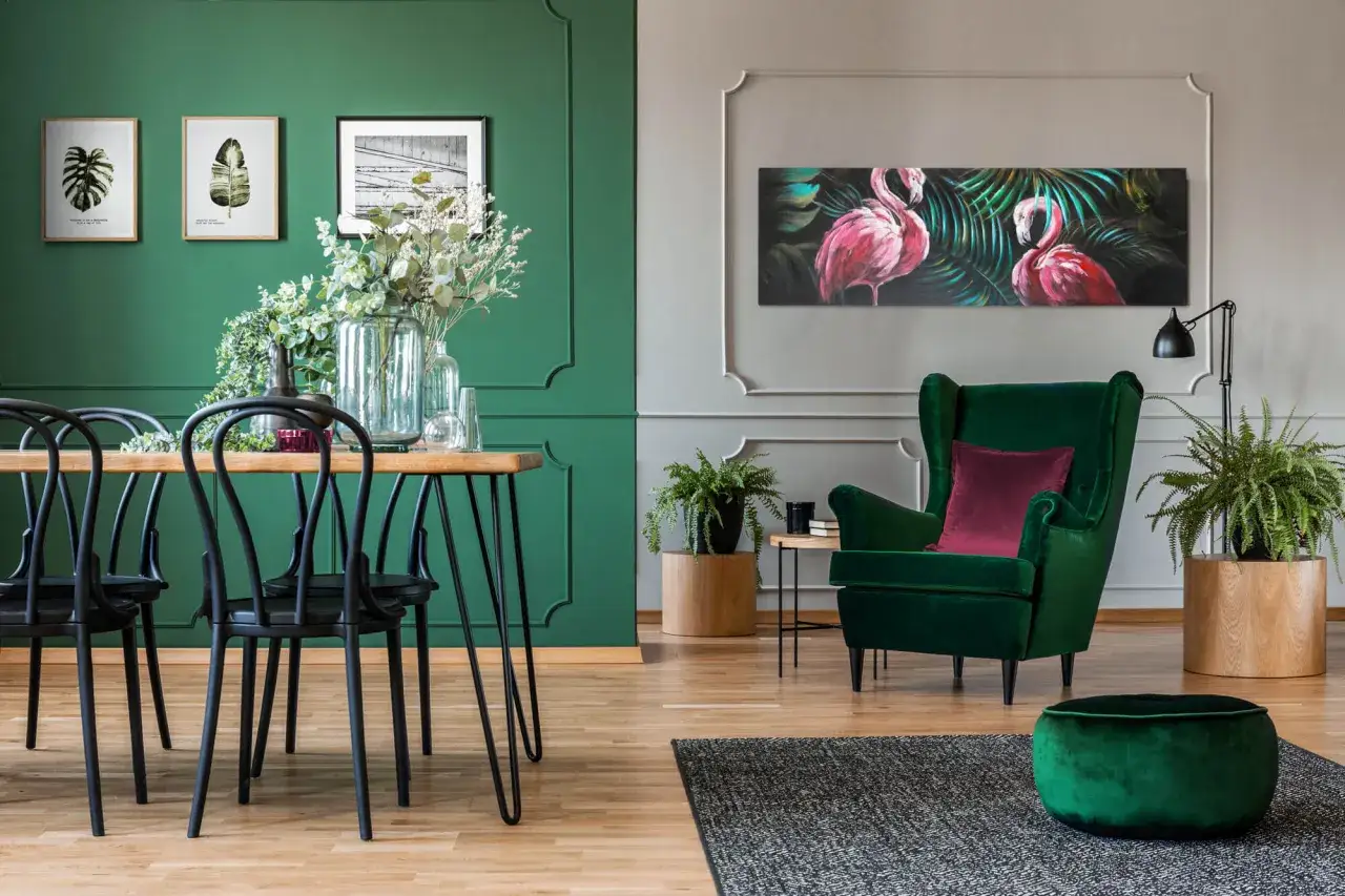 Elegancki salon z fotelem i pufą w kolorze szmaragdowym, obrazem flamingów i zieloną ścianą.